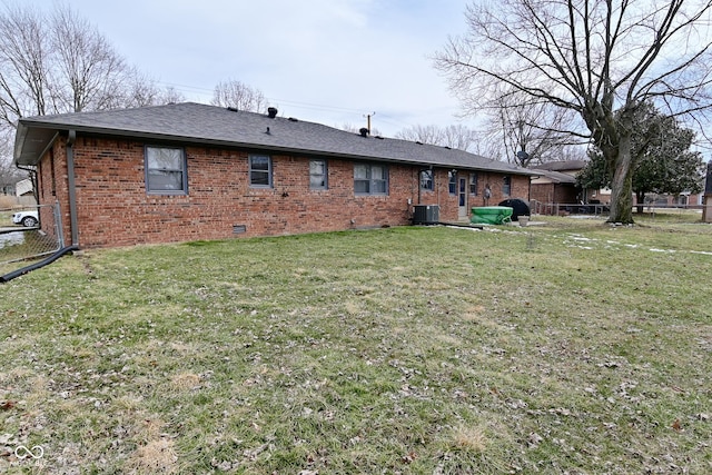 rear view of property with central AC unit, a yard, fence, and brick siding