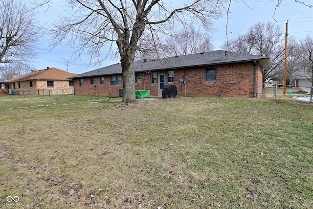 back of property featuring a yard, brick siding, fence, and central air condition unit