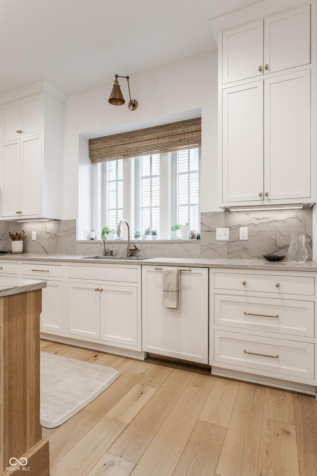 kitchen featuring light wood-style flooring, decorative backsplash, white cabinets, white dishwasher, and a sink