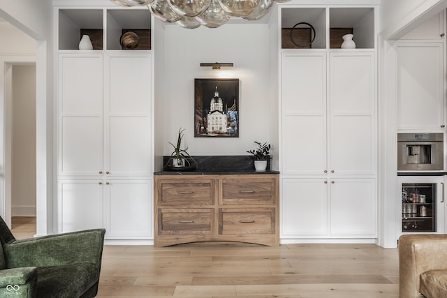 bar featuring light wood-style flooring, stainless steel oven, and beverage cooler