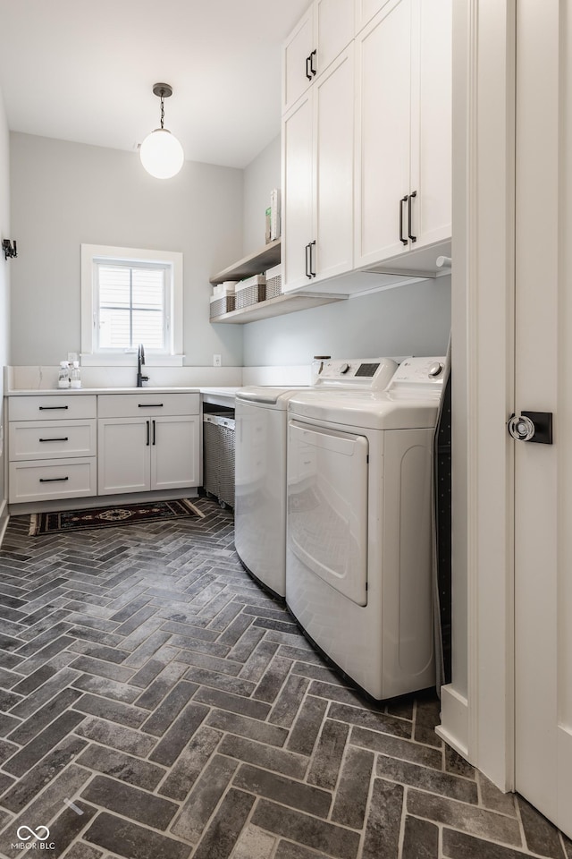 laundry room with brick floor, cabinet space, a sink, and washing machine and clothes dryer