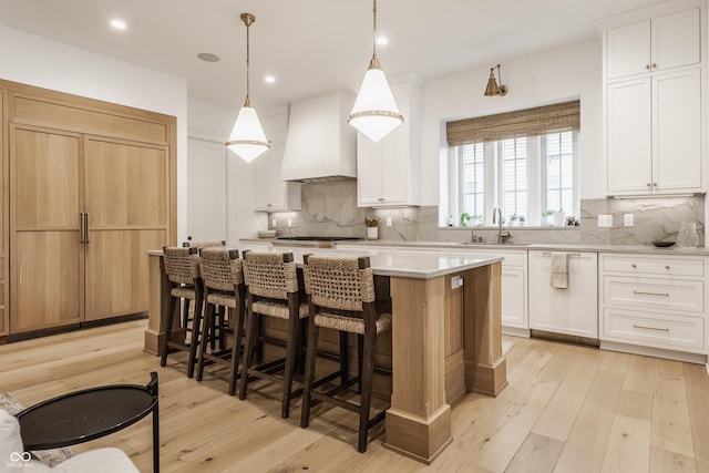 kitchen with dishwasher, a sink, custom exhaust hood, light wood-type flooring, and backsplash