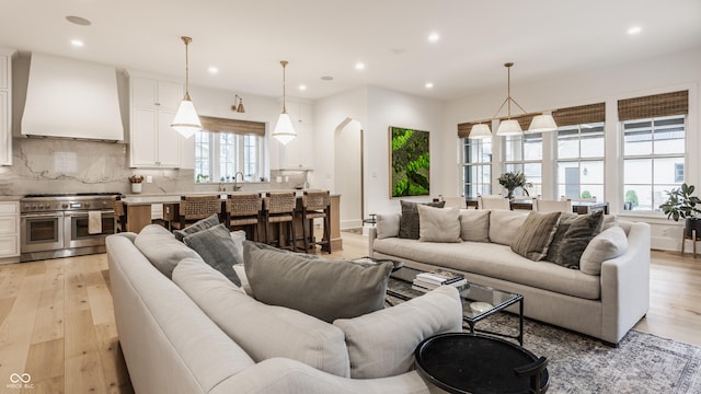 living area with arched walkways, recessed lighting, and light wood-style flooring