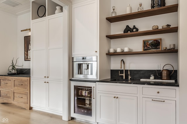 bar featuring oven, beverage cooler, a sink, visible vents, and light wood-type flooring