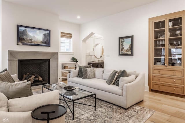 living room featuring light wood-type flooring, a high end fireplace, arched walkways, and recessed lighting