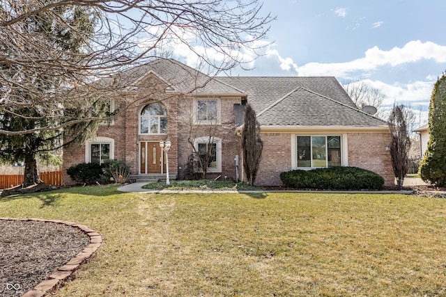 traditional-style house featuring brick siding, a shingled roof, fence, and a front yard