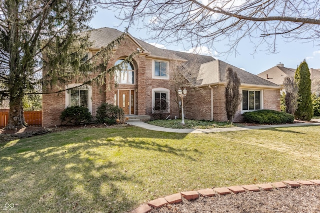 view of front facade featuring brick siding, fence, a front lawn, and roof with shingles