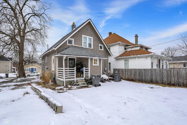 snow covered property featuring a chimney, fence, and a porch