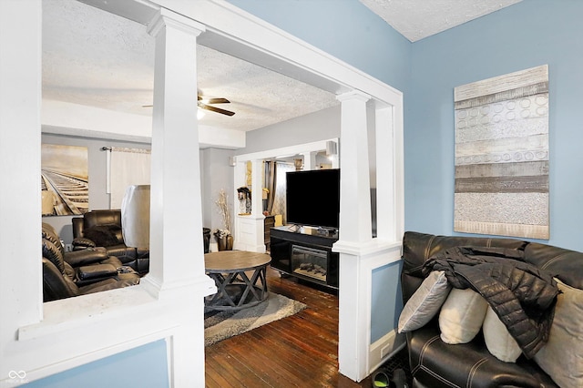 living room with a textured ceiling, a ceiling fan, wood-type flooring, a glass covered fireplace, and decorative columns