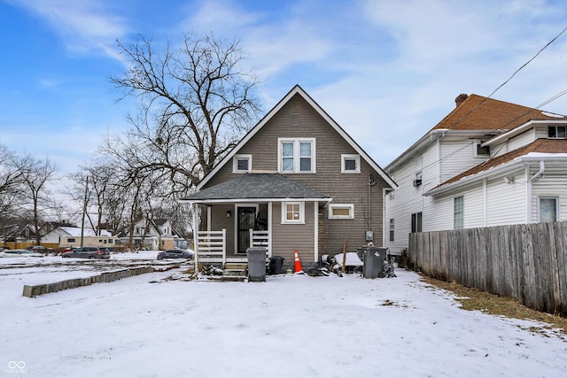 snow covered property featuring covered porch and fence