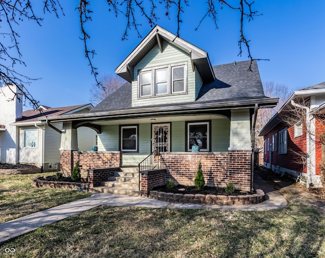 bungalow featuring brick siding, covered porch, and a front yard