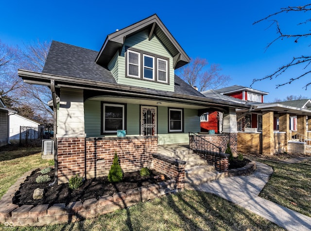 view of front of house with brick siding, a porch, roof with shingles, and fence