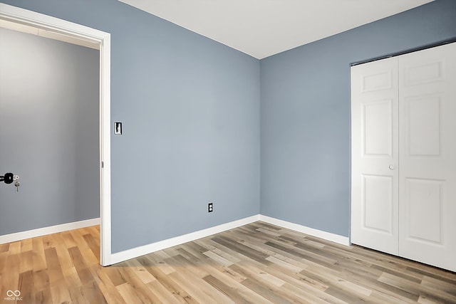 unfurnished bedroom featuring light wood finished floors, a closet, and baseboards