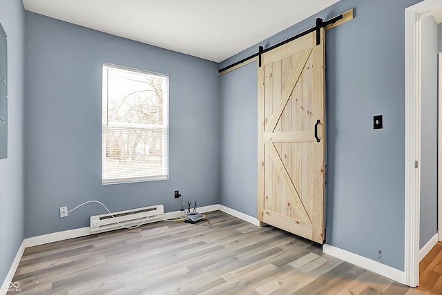 unfurnished bedroom with baseboards, a barn door, a baseboard heating unit, and wood finished floors