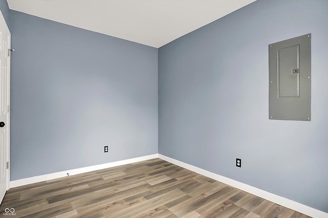 empty room featuring wood finished floors, electric panel, and baseboards