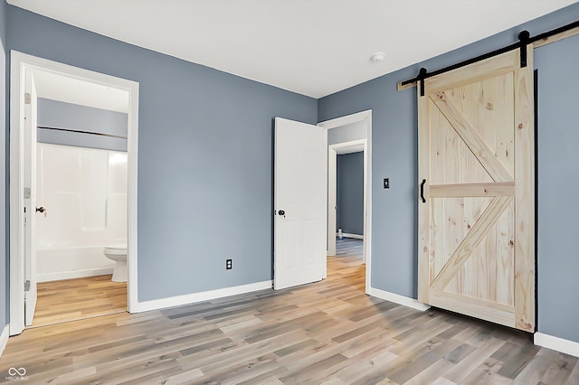 unfurnished bedroom with light wood-style floors, ensuite bathroom, baseboards, and a barn door