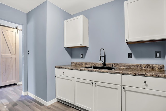 kitchen with white cabinetry, a sink, light wood-style flooring, and a barn door
