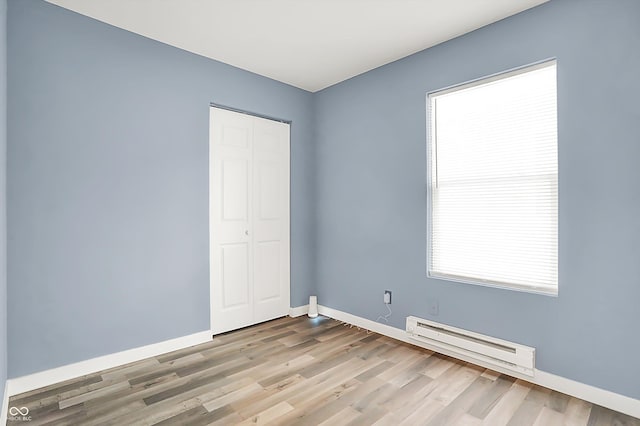 empty room with a baseboard heating unit, baseboards, and wood finished floors