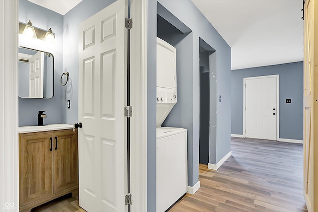 clothes washing area with stacked washer / drying machine, light wood-style floors, a sink, laundry area, and baseboards