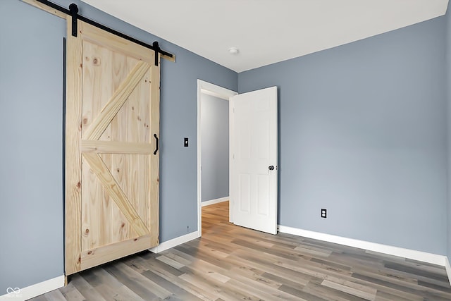 unfurnished room with wood finished floors, baseboards, and a barn door