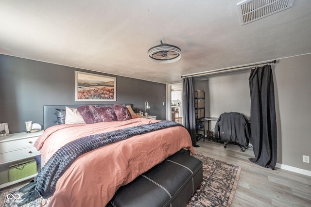 bedroom with wood finished floors, visible vents, and baseboards