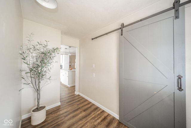 hallway featuring dark wood-style floors, a barn door, and baseboards