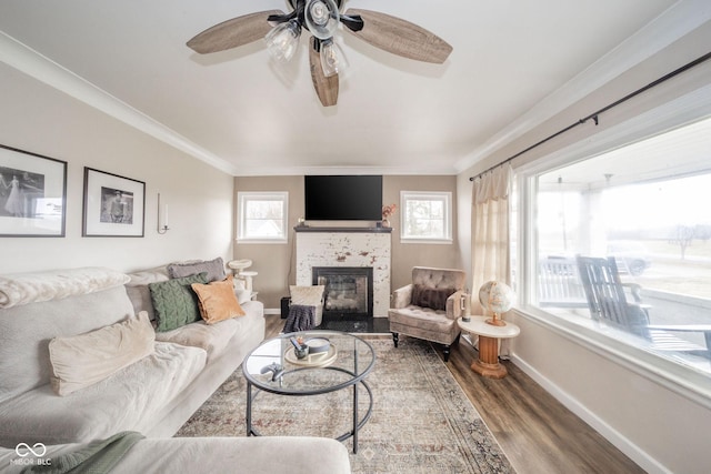 living room featuring a tiled fireplace, baseboards, crown molding, and wood finished floors