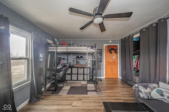 bedroom featuring multiple windows, ceiling fan, baseboards, and wood finished floors