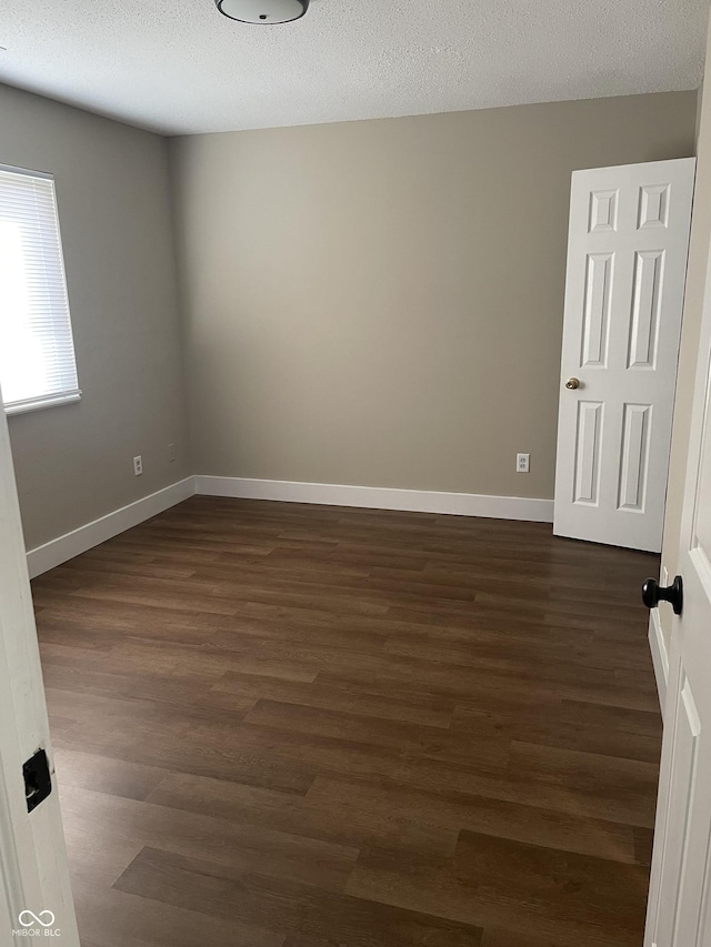 unfurnished room with a textured ceiling, dark wood-type flooring, and baseboards