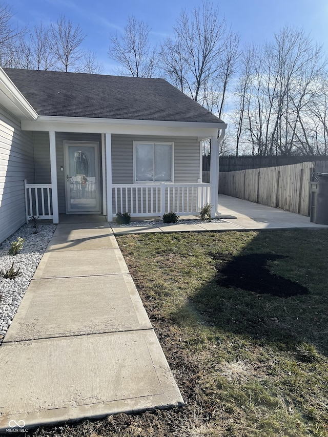 property entrance featuring fence, a porch, and roof with shingles