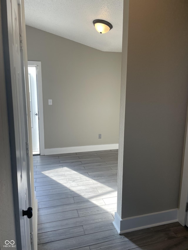 empty room with a textured ceiling, baseboards, vaulted ceiling, and wood finished floors