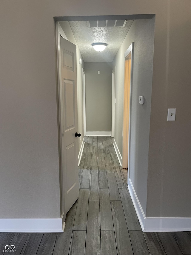 corridor with a textured ceiling, baseboards, visible vents, and wood tiled floor