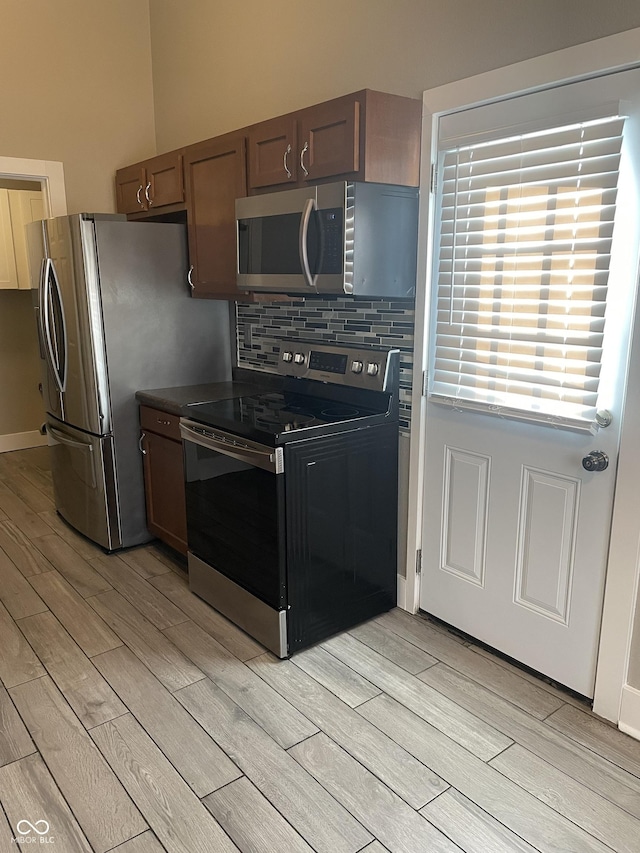 kitchen featuring wood finish floors, stainless steel appliances, dark countertops, backsplash, and baseboards