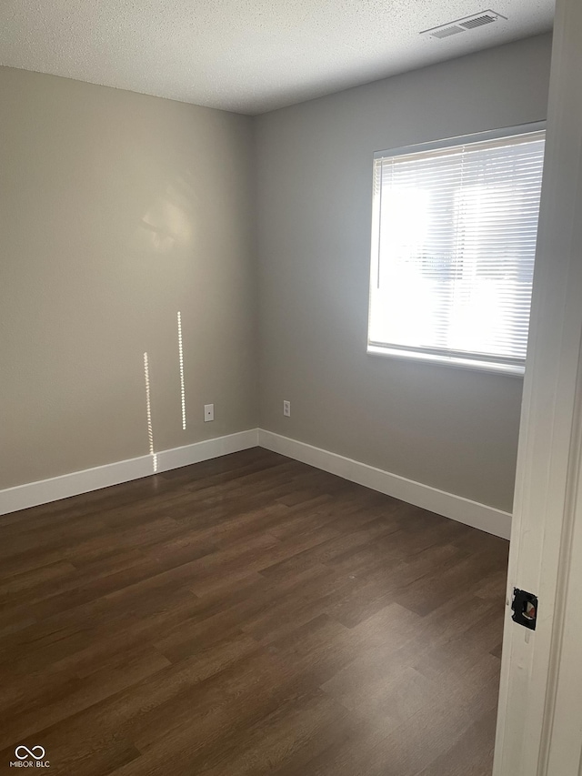 unfurnished room featuring a textured ceiling, dark wood finished floors, visible vents, and baseboards