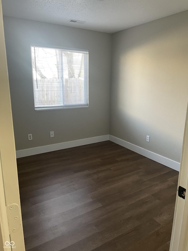 unfurnished room with visible vents, dark wood finished floors, a textured ceiling, and baseboards