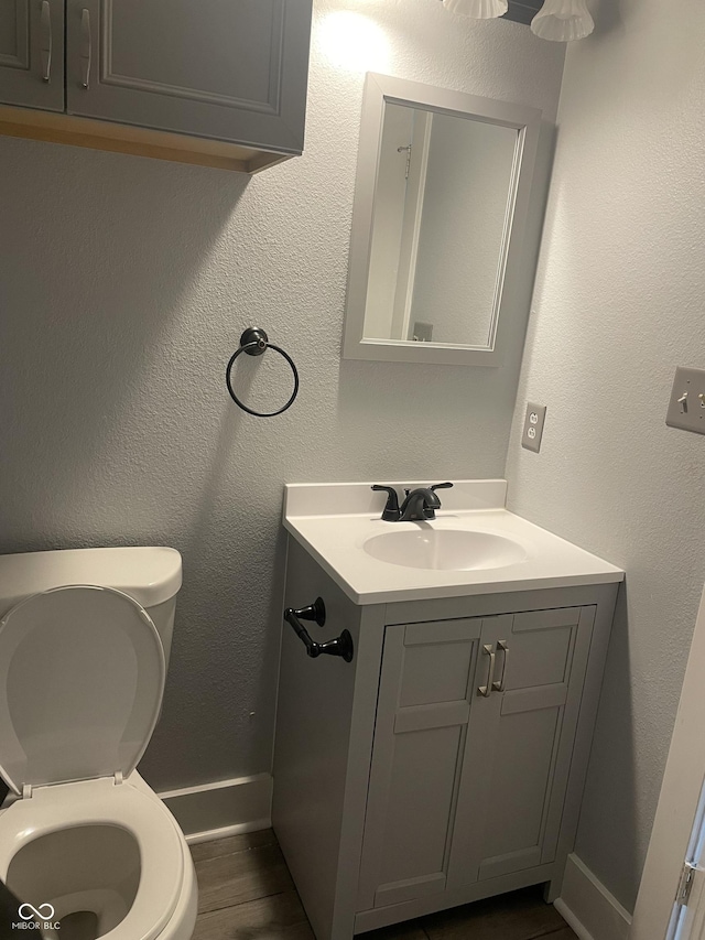 bathroom featuring a textured wall, toilet, wood finished floors, vanity, and baseboards