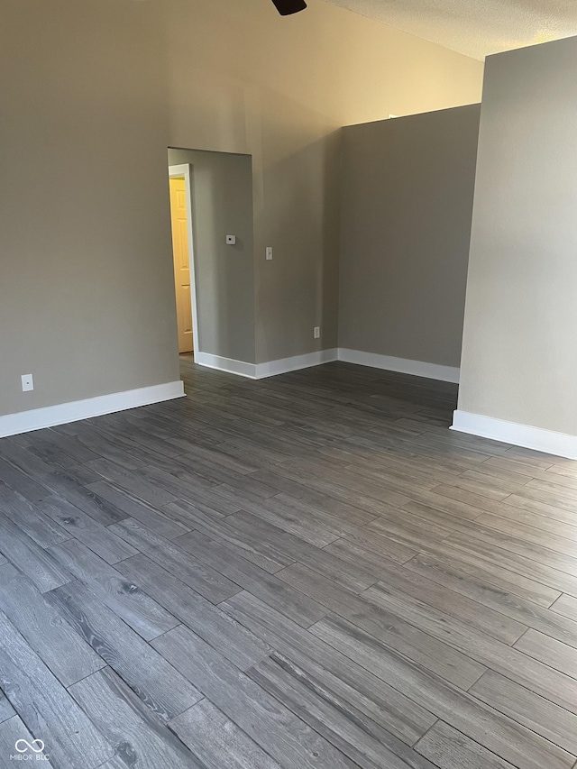 spare room featuring vaulted ceiling, dark wood-style flooring, a textured ceiling, and baseboards