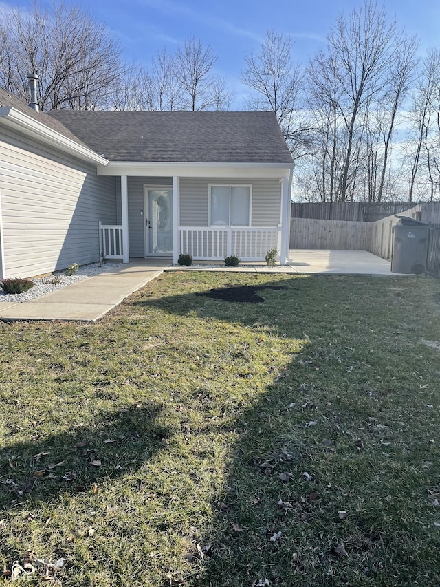 property entrance with a porch, fence, a shingled roof, and a lawn