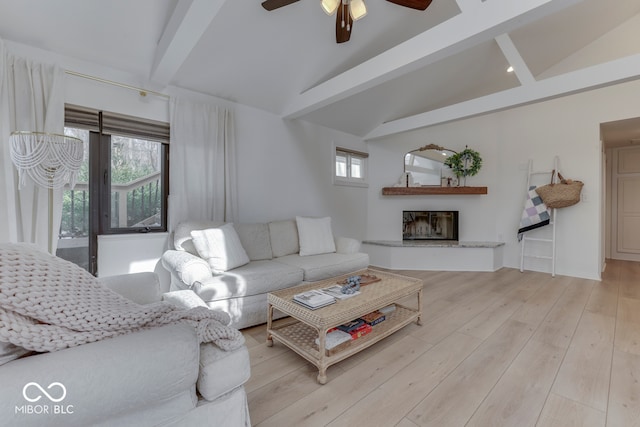 living room featuring vaulted ceiling with beams, a fireplace with raised hearth, a healthy amount of sunlight, and light wood-style floors