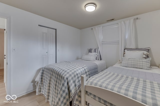 bedroom with a closet, visible vents, light wood-style flooring, and baseboards