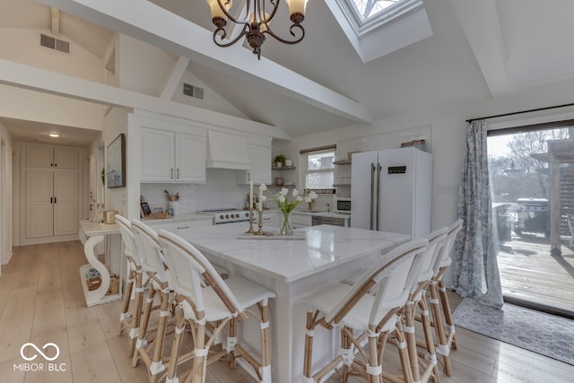 kitchen featuring visible vents, hanging light fixtures, white cabinetry, a kitchen island, and white appliances