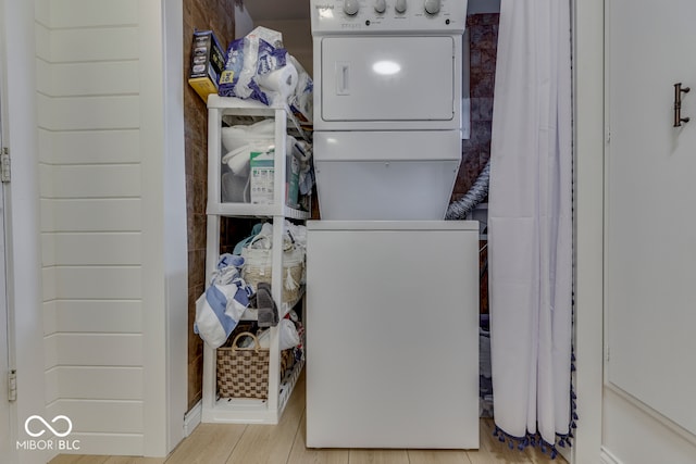 washroom with light wood-type flooring, stacked washing maching and dryer, and laundry area