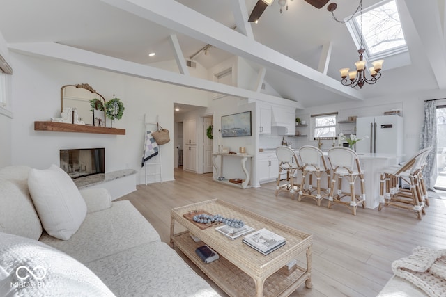 living area featuring a skylight, a glass covered fireplace, light wood-style flooring, high vaulted ceiling, and beam ceiling