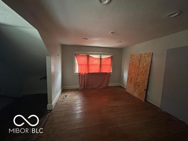 empty room featuring a textured ceiling, baseboards, and wood finished floors