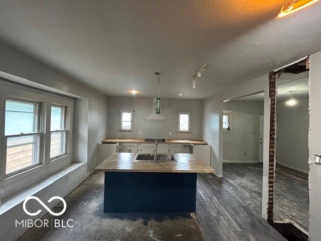 kitchen featuring decorative light fixtures, dark wood finished floors, a center island with sink, light countertops, and a sink