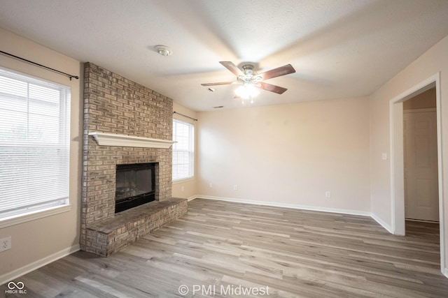 unfurnished living room featuring baseboards, a ceiling fan, light wood-style flooring, a textured ceiling, and a fireplace