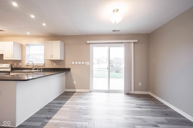 kitchen with white cabinetry, a sink, dark stone countertops, range, and baseboards