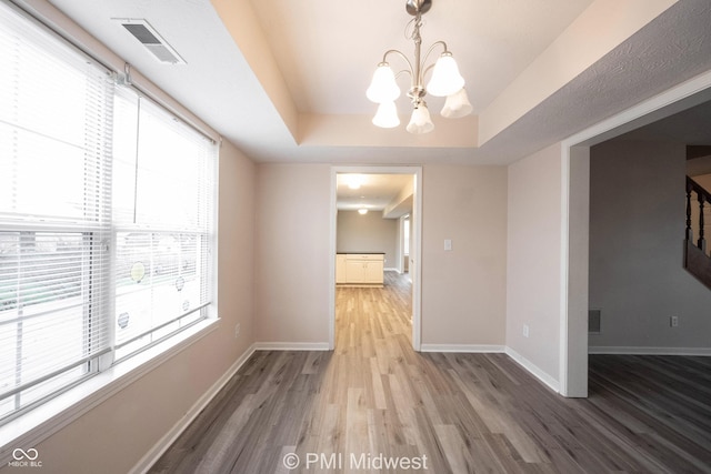 unfurnished dining area with baseboards, visible vents, a raised ceiling, and wood finished floors