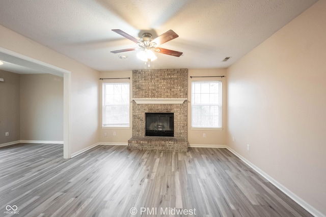 unfurnished living room featuring a fireplace, visible vents, ceiling fan, a textured ceiling, and wood finished floors