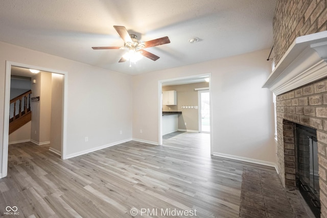 unfurnished living room featuring a brick fireplace, stairs, baseboards, and light wood-style floors